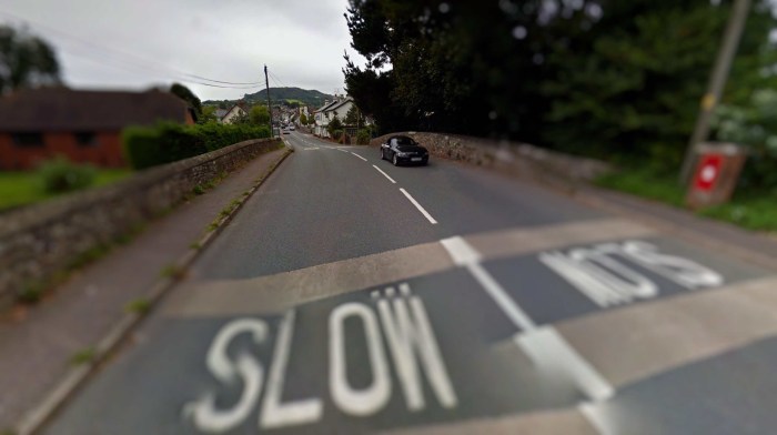 How to pass your UK driving test. Vehicle driving on a road with a slow sign painted on the road